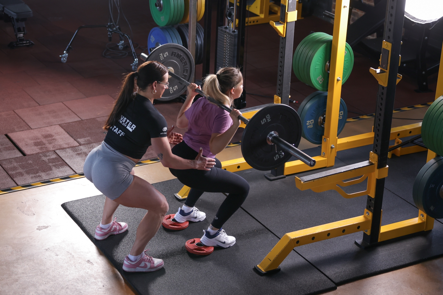 Sportlerin wird von Trainerin bei Squats supportet.